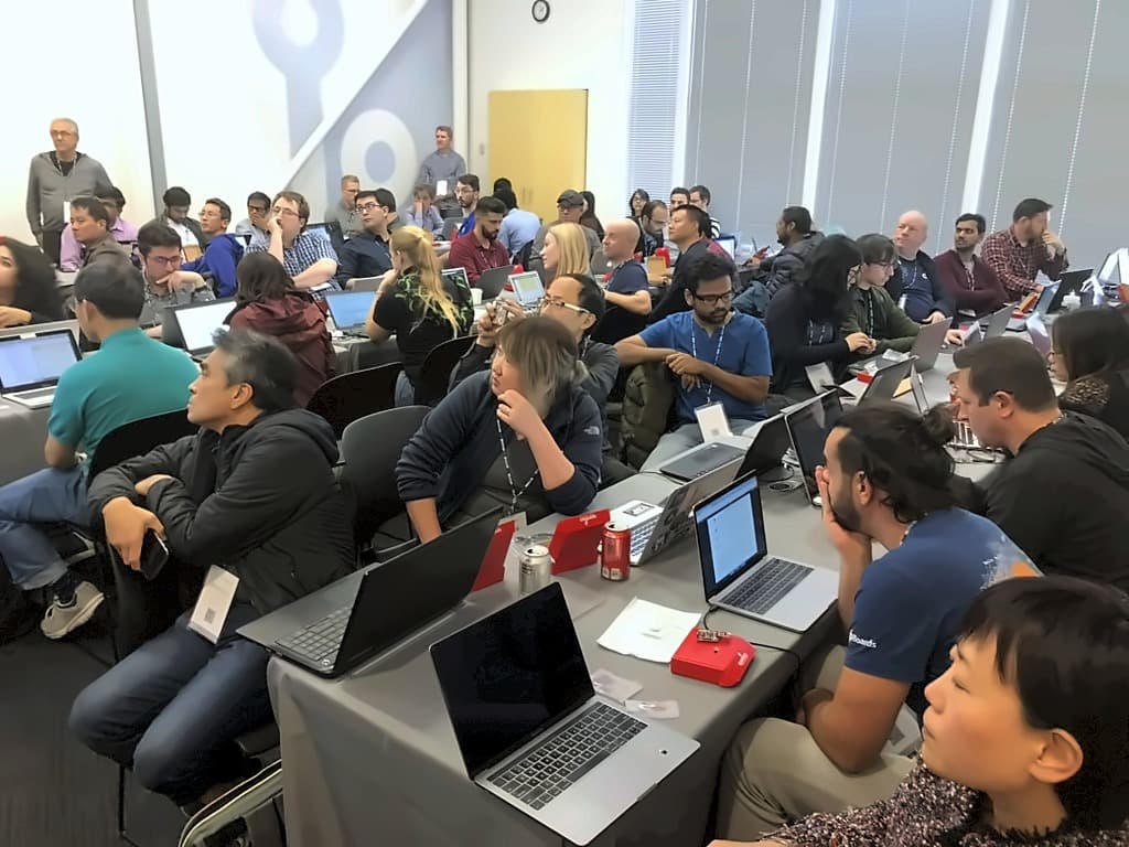 A packed workshop room with every table covered in open laptops and development boards