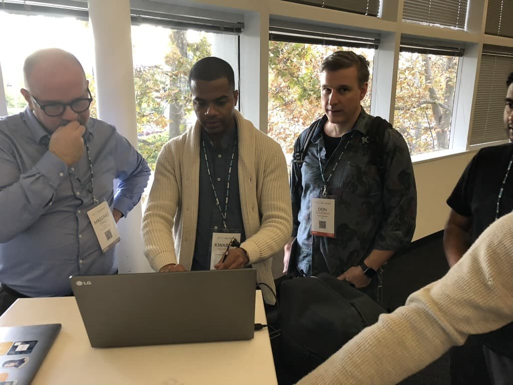 Four attendees gathered around a laptop working through a problem together during a break