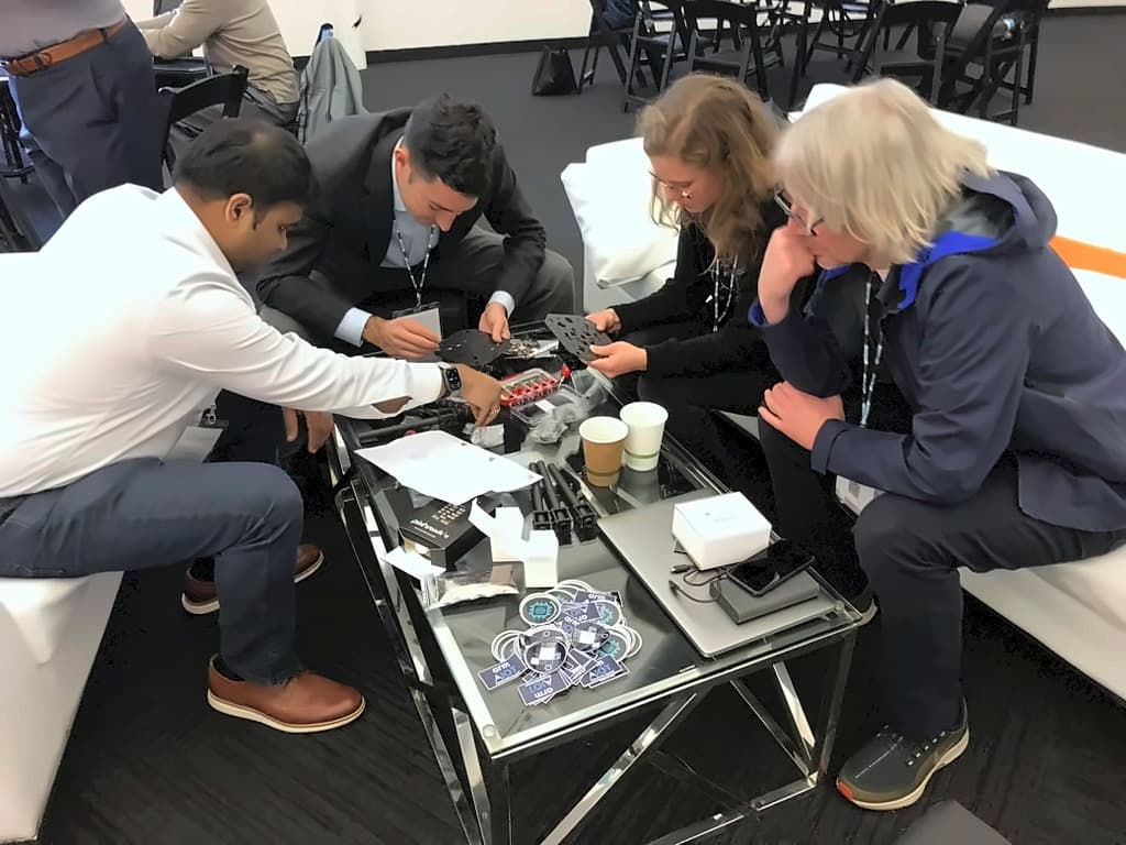 Attendees in the lounge assembling a drone frame on a coffee table scattered with components and Arm stickers