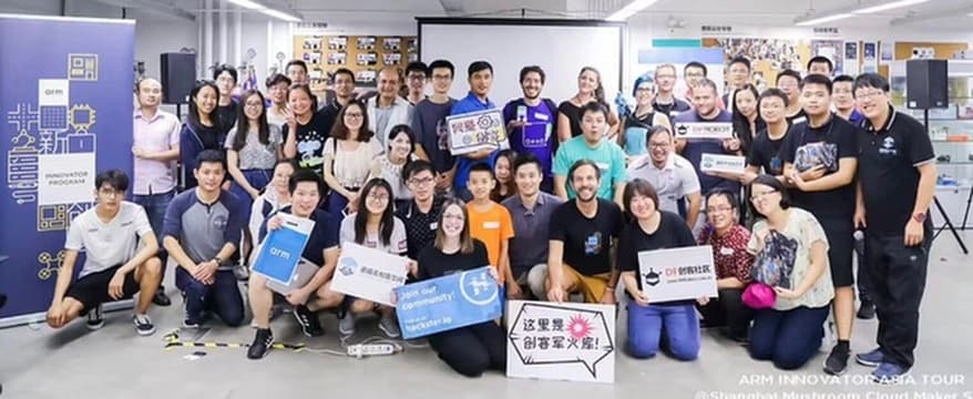 About fifty attendees in a group photo beside an Arm Innovator Program banner, several holding signs including one reading Join our community! hackster.io