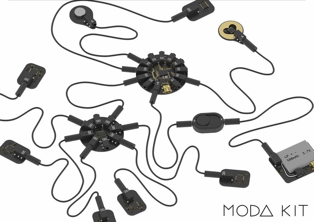 The MODA Kit product render — two circular hub boards with radiating connectors, linked by soft black cables to sensor pods, a switch and a lithium cell