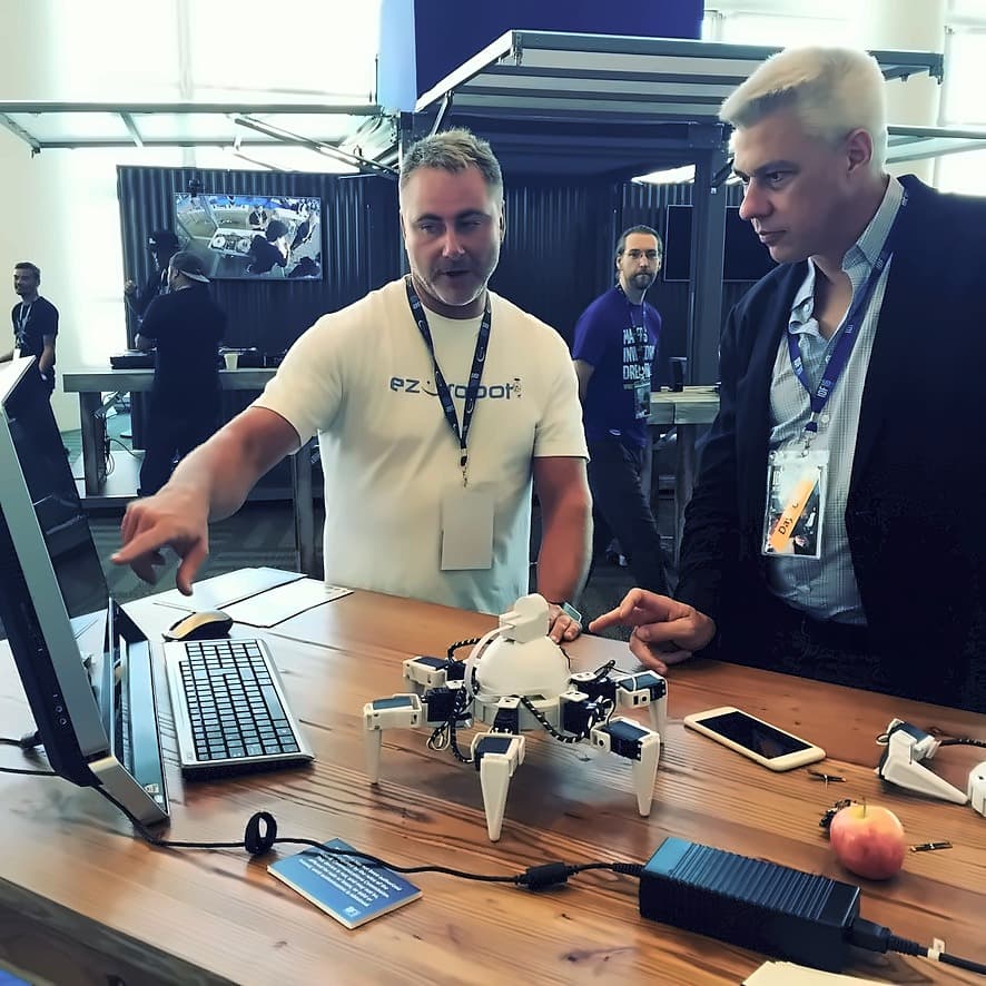 An EZ-Robot engineer demonstrating a six-legged Joule-powered hexapod to an attendee across the demo table