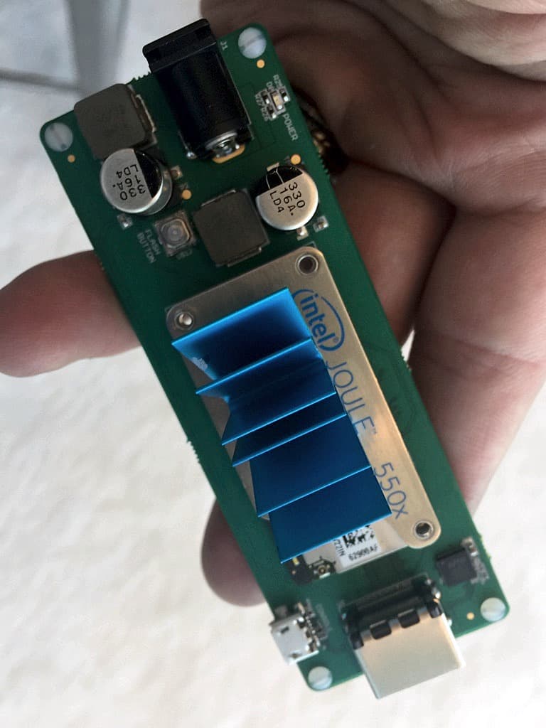 An Intel Joule 550x module with its blue finned heatsink, seated on a small carrier board with a barrel jack, micro USB and ethernet, held in one hand